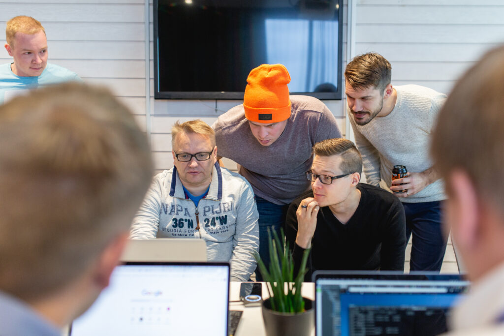 WeAre Solutions team members gathered around a laptop during a collaborative work session in 2018, discussing and reviewing something on the screen.